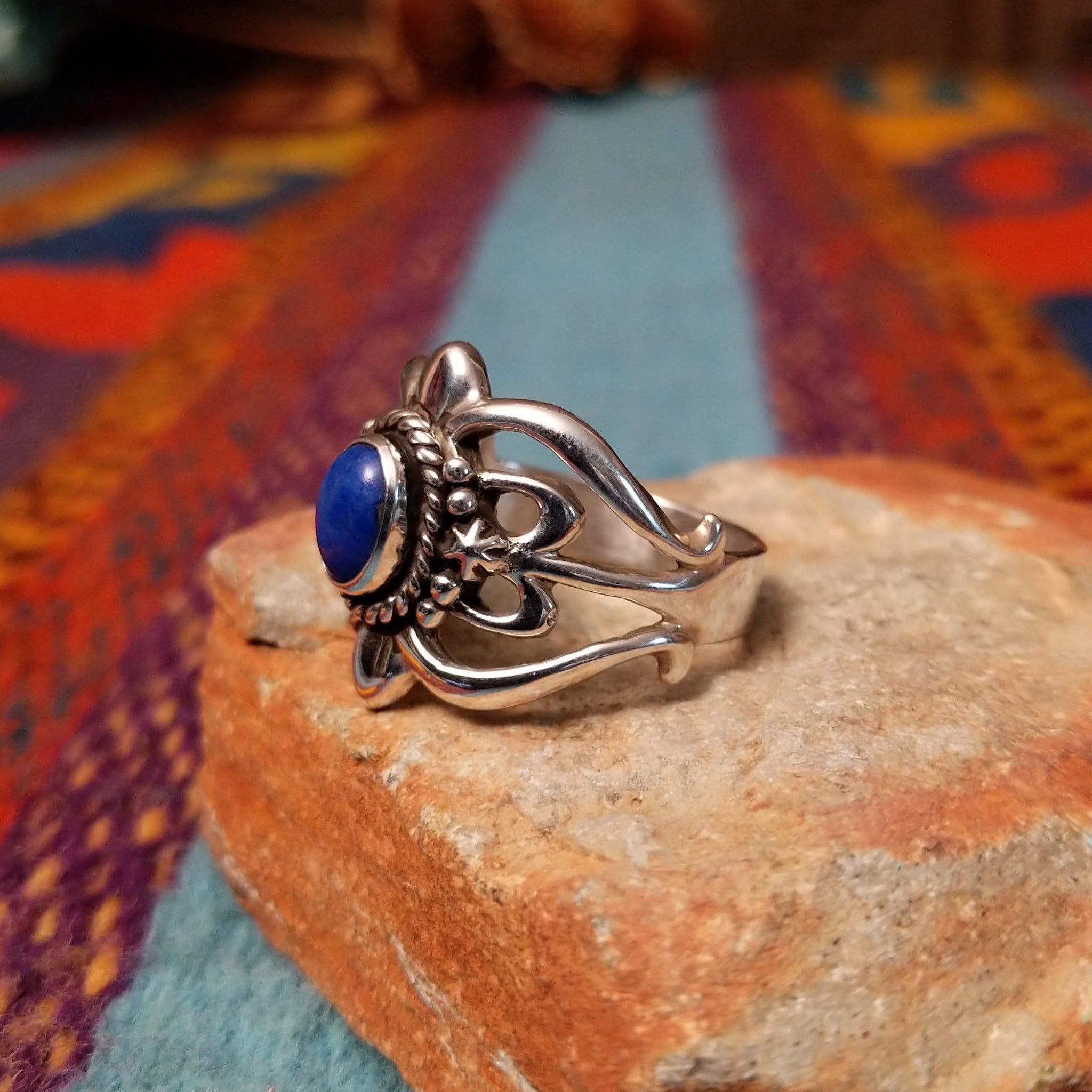 Ornate Lapis Ring by Raymond Coriz featuring an oval blue lapis stone set in Sterling Silver with twisted rope, polished bead accents, sculpted details, and decorative openwork; side view.