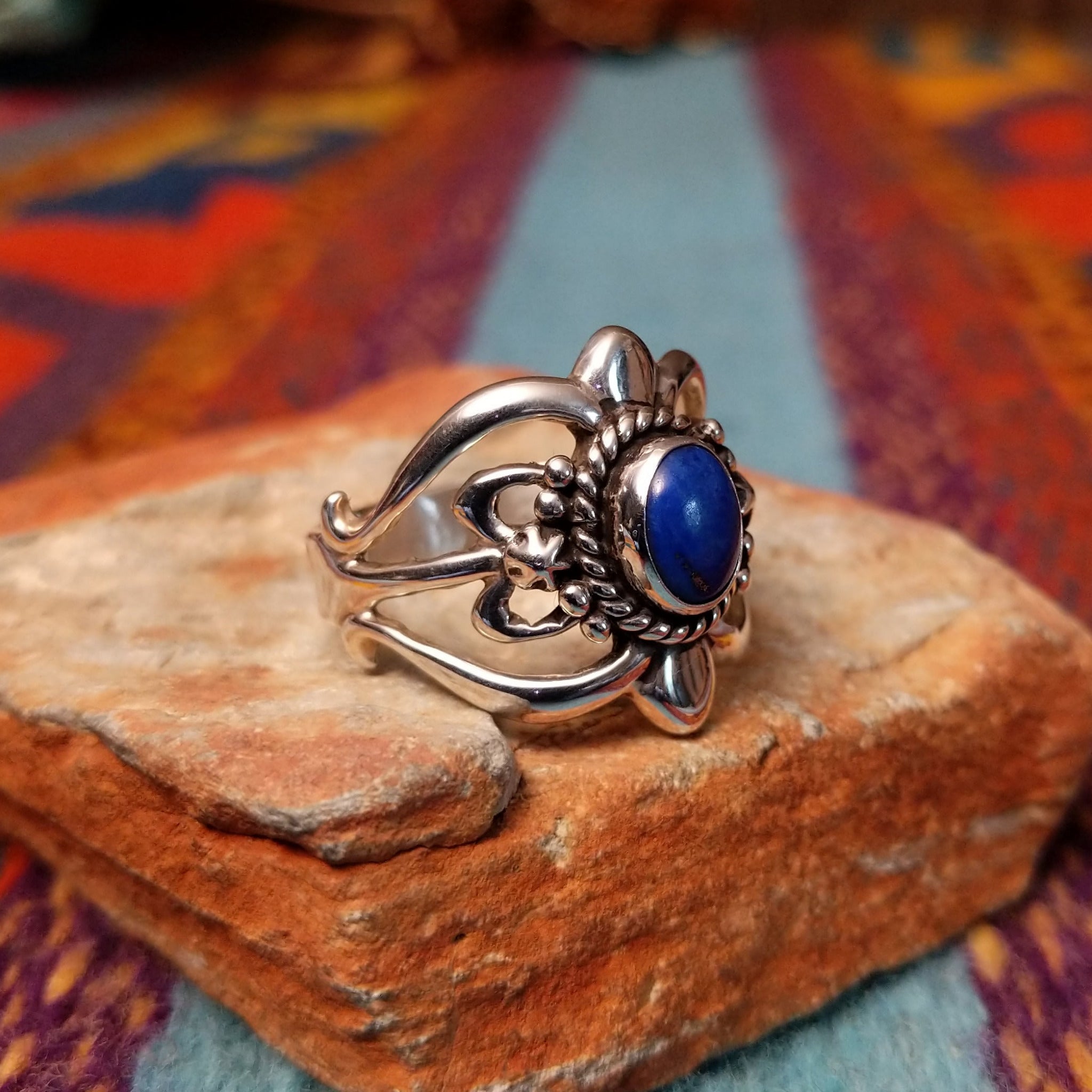Ornate Lapis Ring by Raymond Coriz featuring an oval blue lapis stone set in Sterling Silver with twisted rope, polished bead accents, sculpted details, and decorative openwork; side view.