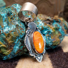 Sterling silver pendant with orange spiny oyster shell set in an oval bezel, framed by ornate silverwork.