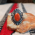 Ornate red spiny oyster shell ring by Raymond Coriz featuring an oval red-orange shell cabochon surrounded by twisted rope, fan-shaped silverwork, scrolls, and decorative silver beads.