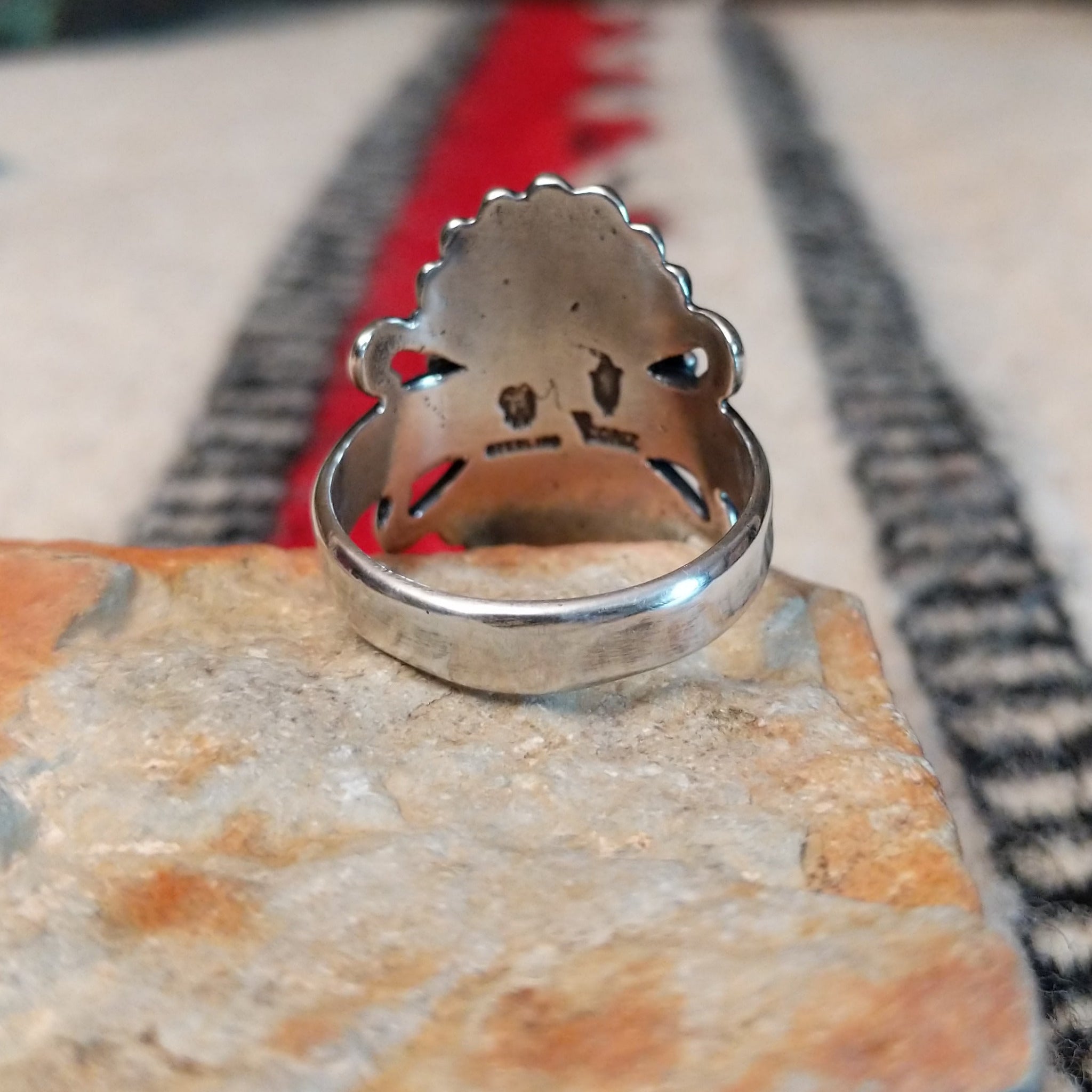 Ornate red spiny oyster shell ring by Raymond Coriz featuring an oval red-orange shell cabochon surrounded by twisted rope, fan-shaped silverwork, scrolls, and decorative silver beads; underside view.