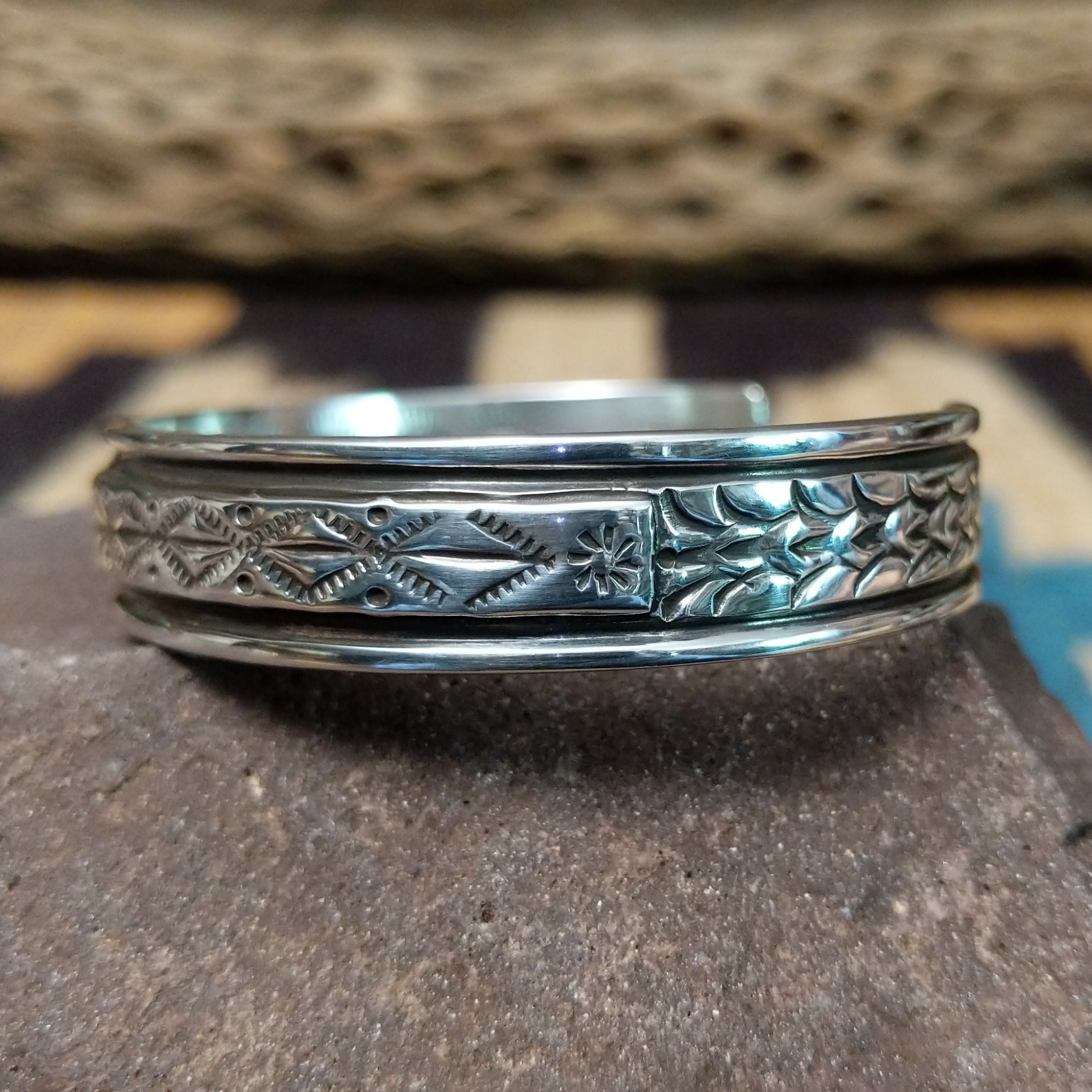 Ornate stamped sterling silver cuff by Diane Wylie, featuring intricate geometric hand-stamped patterns framed by polished silver borders in a handcrafted open cuff design.