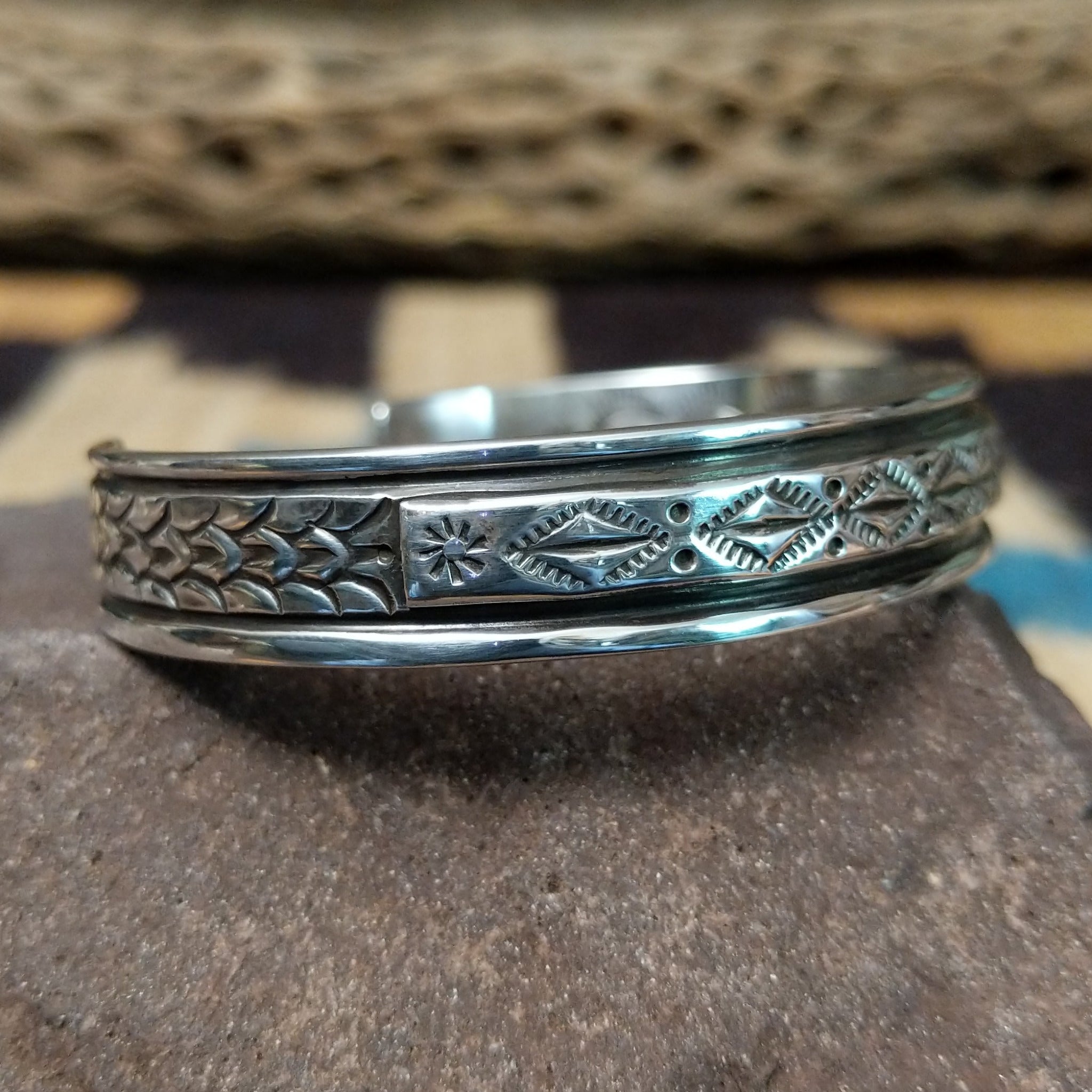 Ornate stamped sterling silver cuff by Diane Wylie, featuring intricate geometric hand-stamped patterns framed by polished silver borders in a handcrafted open cuff design.