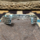 Ornate stamped sterling silver cuff by Diane Wylie, featuring intricate geometric hand-stamped patterns framed by polished silver borders in a handcrafted open cuff design.  Underside view.