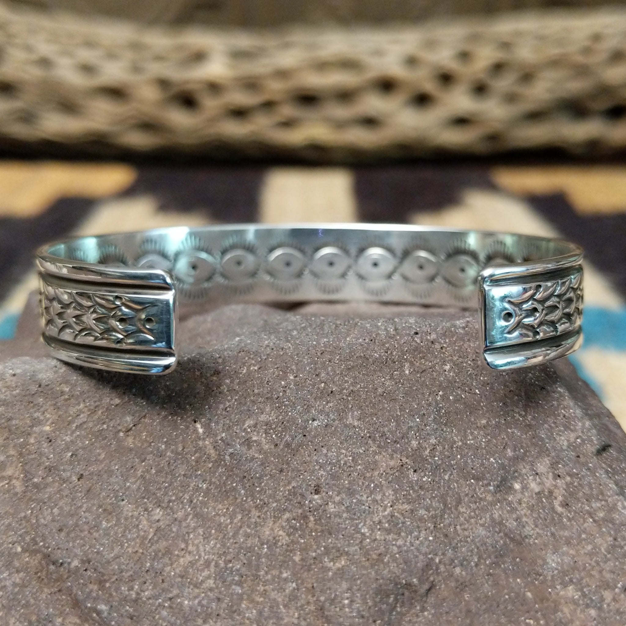 Ornate stamped sterling silver cuff by Diane Wylie, featuring intricate geometric hand-stamped patterns framed by polished silver borders in a handcrafted open cuff design.  Underside view.
