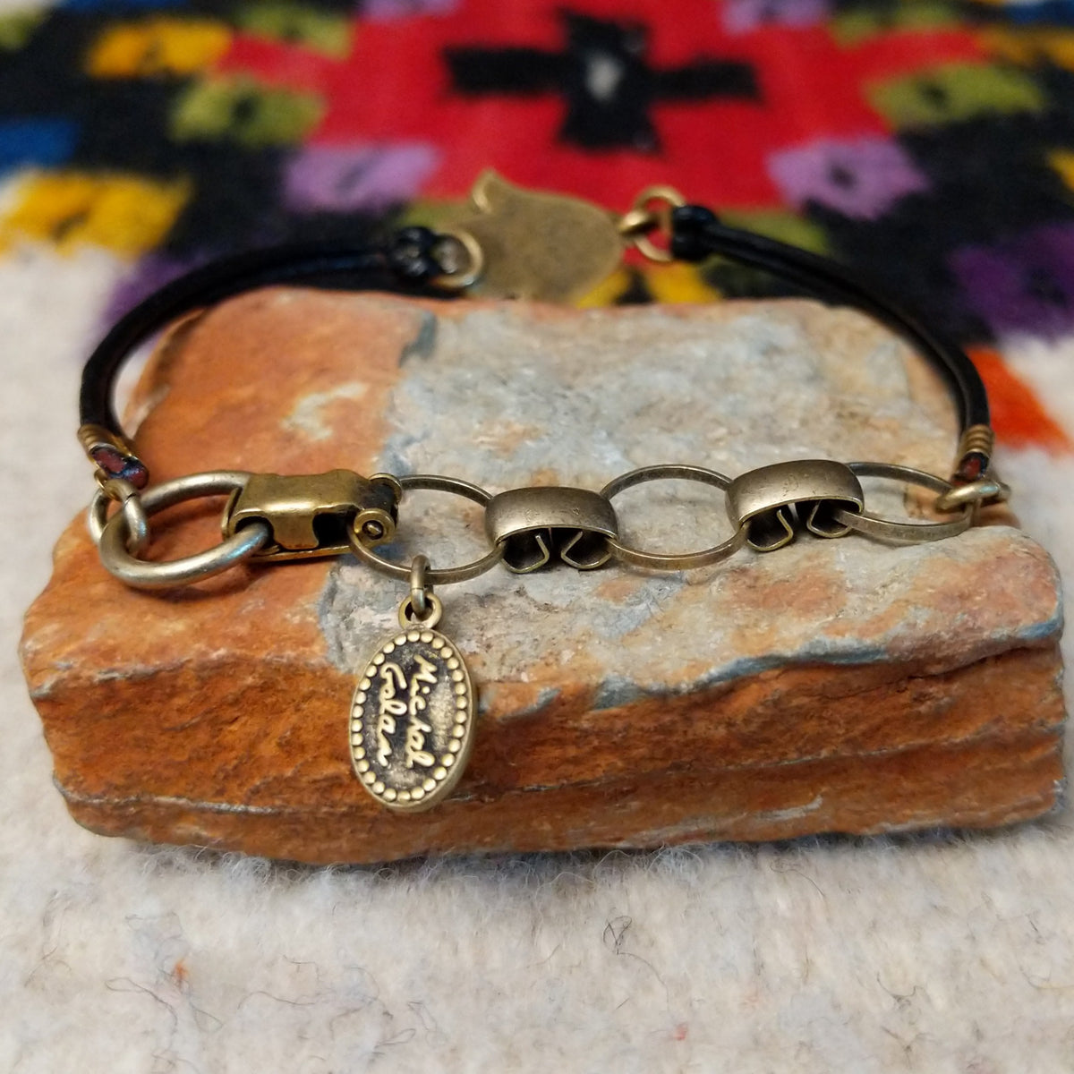 Ornate Hamsa bracelet with a turquoise-colored centerpiece, antique-gold scrollwork, blue crystal accents, and a double-strand black leather cord; artisan tag and clasp view.