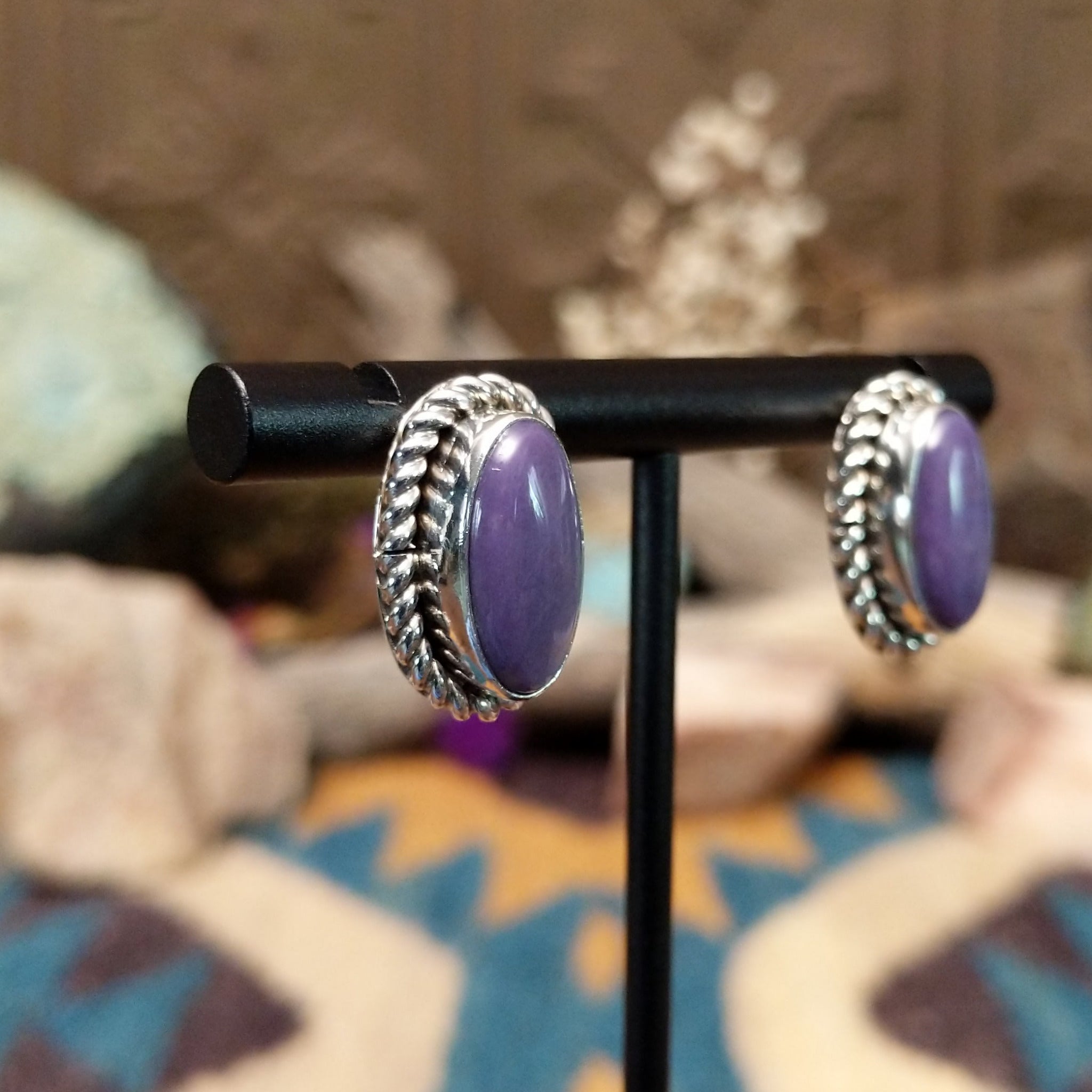 Handcrafted sterling silver post earrings by Priscilla Smith featuring oval charoite cabochons in polished bezel settings with traditional twisted rope border detailing; side view.