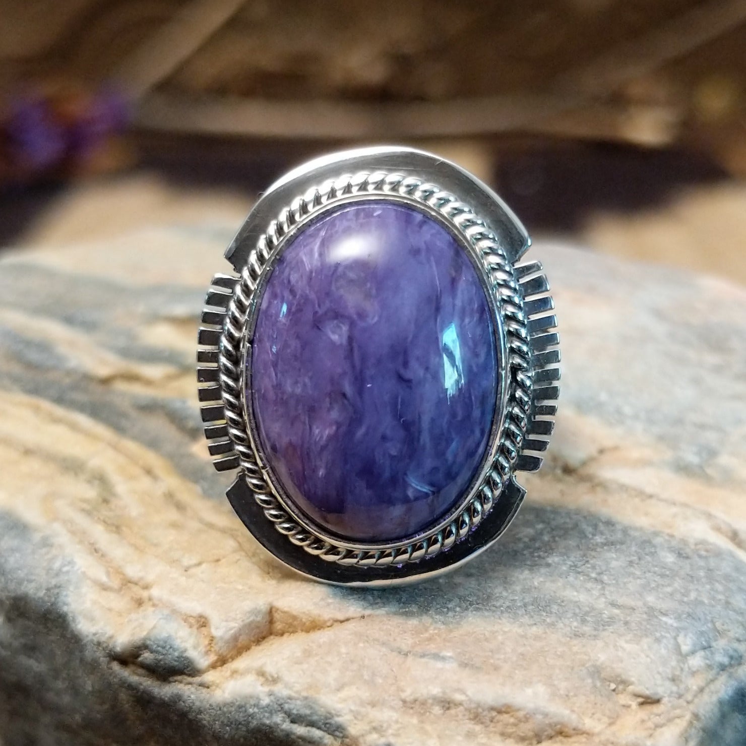 Sterling silver ring with large charoite stone set in an oval bezel, framed by twisted rope and stamped setting.