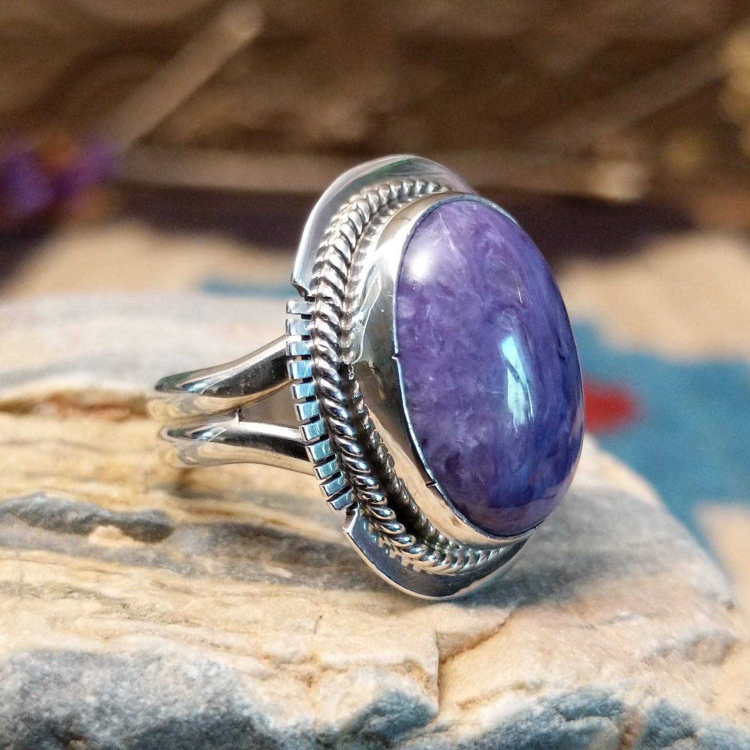 Sterling silver ring with large charoite stone set in an oval bezel, framed by twisted rope and stamped setting.