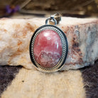 Sterling silver pendant with rhodochrosite set in an oval bezel, framed by twisted rope accents and ledge.