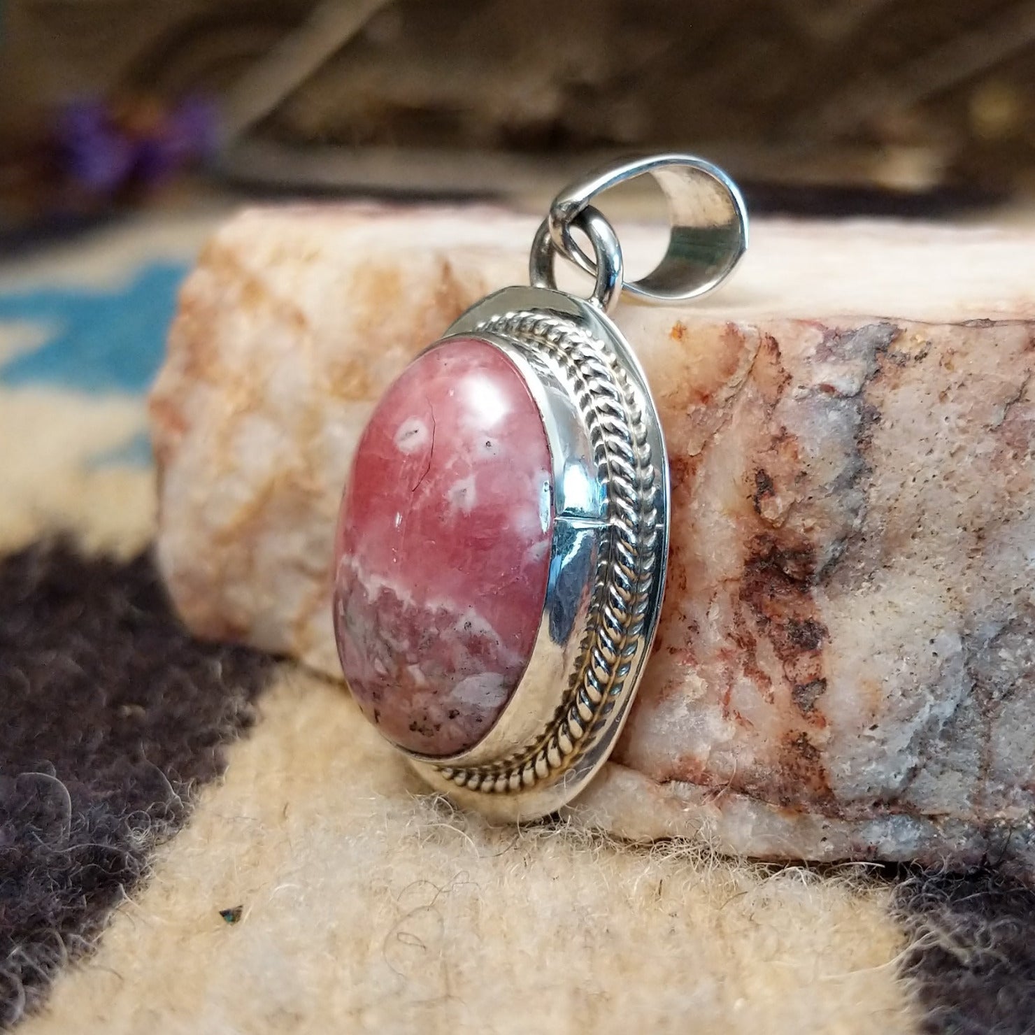 Sterling silver pendant with rhodochrosite set in an oval bezel, framed by twisted rope accents and ledge.