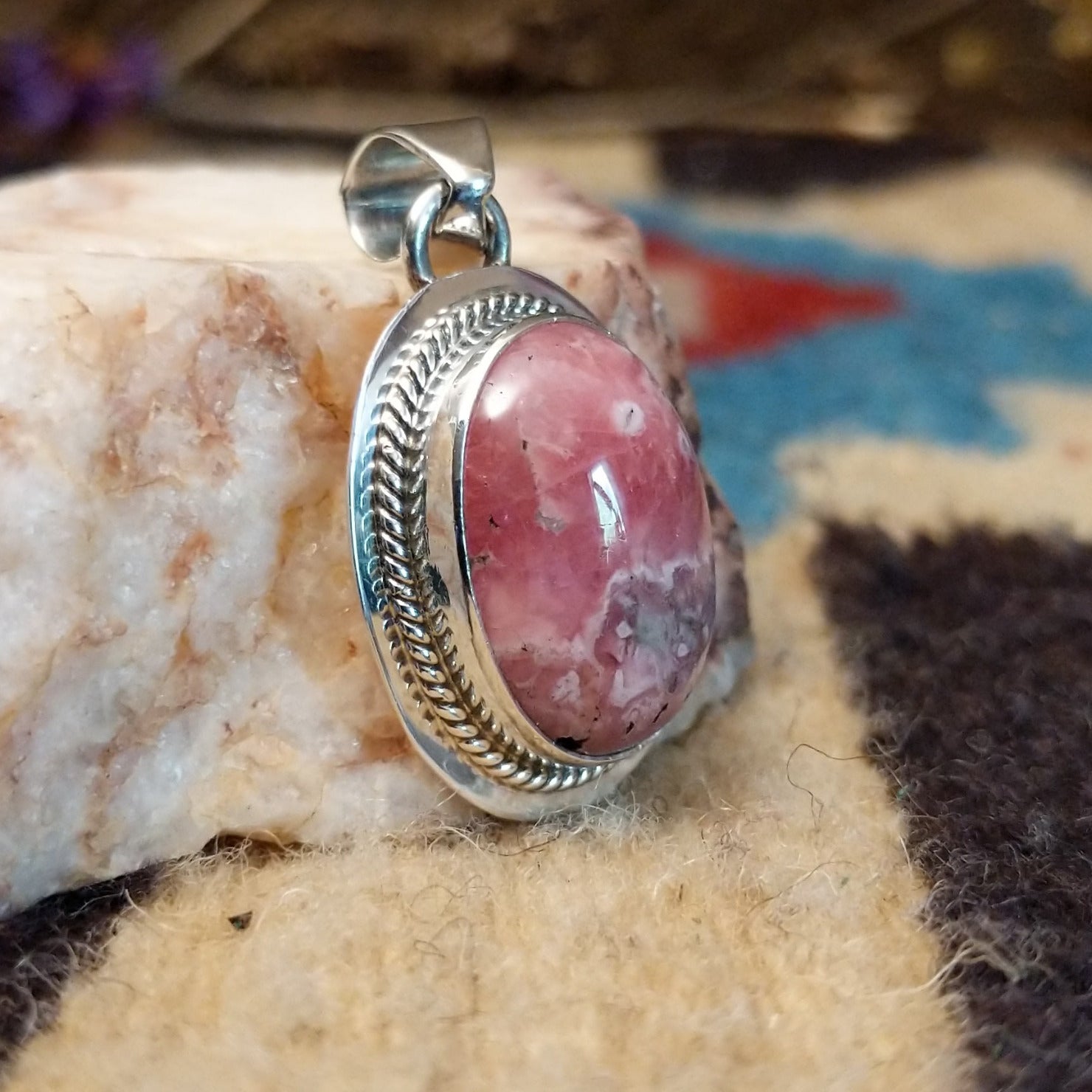 Sterling silver pendant with rhodochrosite set in an oval bezel, framed by twisted rope accents and ledge.