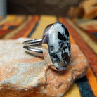 This distinctive Oval White Buffalo Ring by Everett & Mary Teller features a large oval white stone with bold black matrix patterns set in a smooth silver bezel; side view.