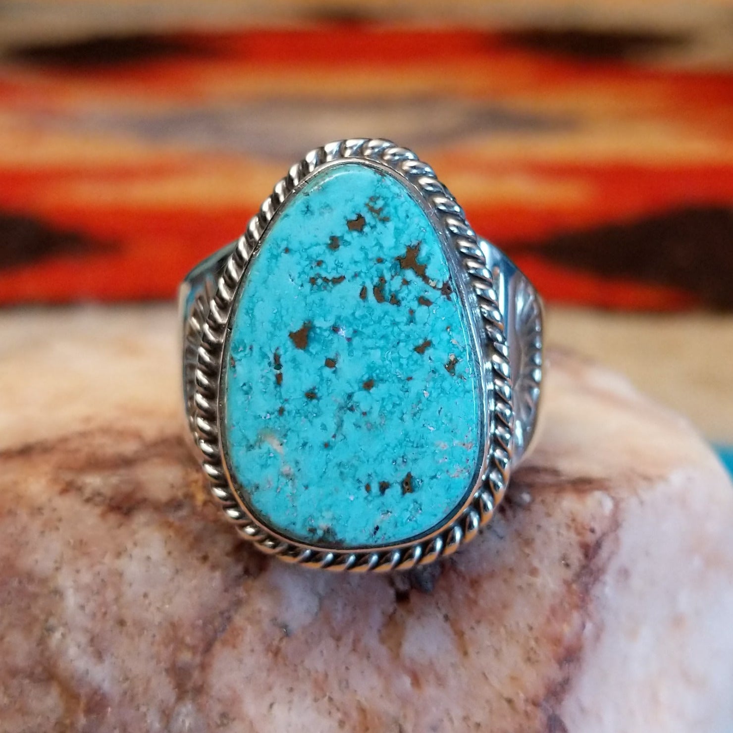 Sterling silver ring with turquoise set in an ovoid setting, framed by twisted rope accents.
