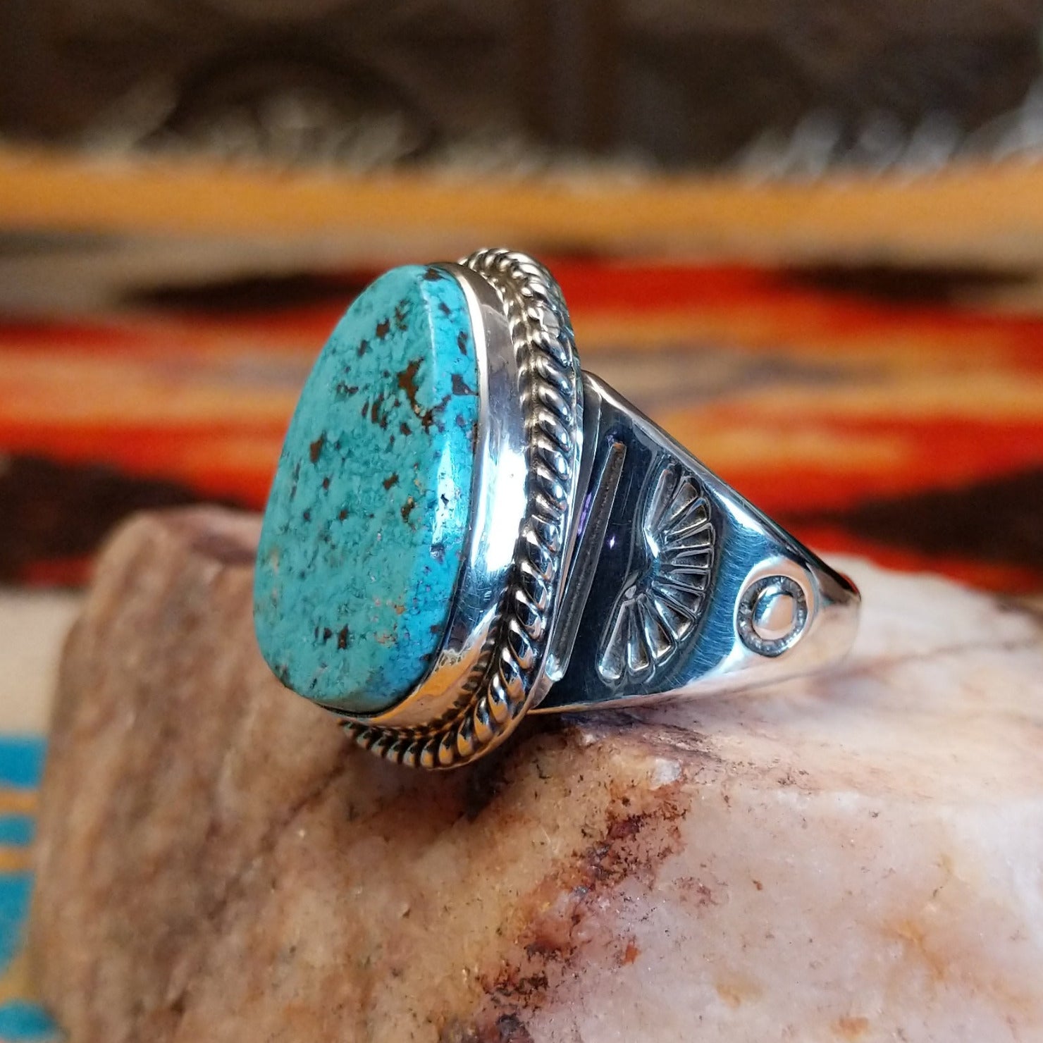 Sterling silver ring with turquoise set in an ovoid setting, framed by twisted rope accents.