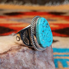 Sterling silver ring with turquoise set in an ovoid setting, framed by twisted rope accents.