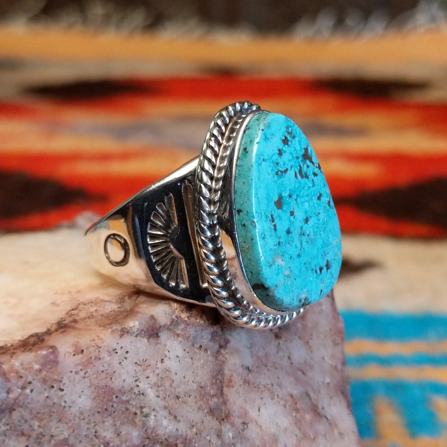 Sterling silver ring with turquoise set in an ovoid setting, framed by twisted rope accents.