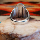Sterling silver ring with turquoise set in an ovoid setting, framed by twisted rope accents.