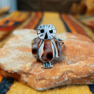 Front view of an owl-shaped silver ring by Regina Kallestewa featuring black circular eyes, engraved facial markings, three brown and white shell inlays, and small silver feet.