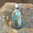 Handcrafted by Navajo artisan L.J., this capsule-shaped pendant features genuine #8 Turquoise set in sterling silver with a rope design accent.