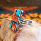 Size 10 ring by Wilbert Grey showcases an inlay design set in sterling silver. The rectangular face features a striking mosaic of vibrant stones, including rich red and orange spiney oyster shell, bright turquoise, and deep blue lapis. Side View