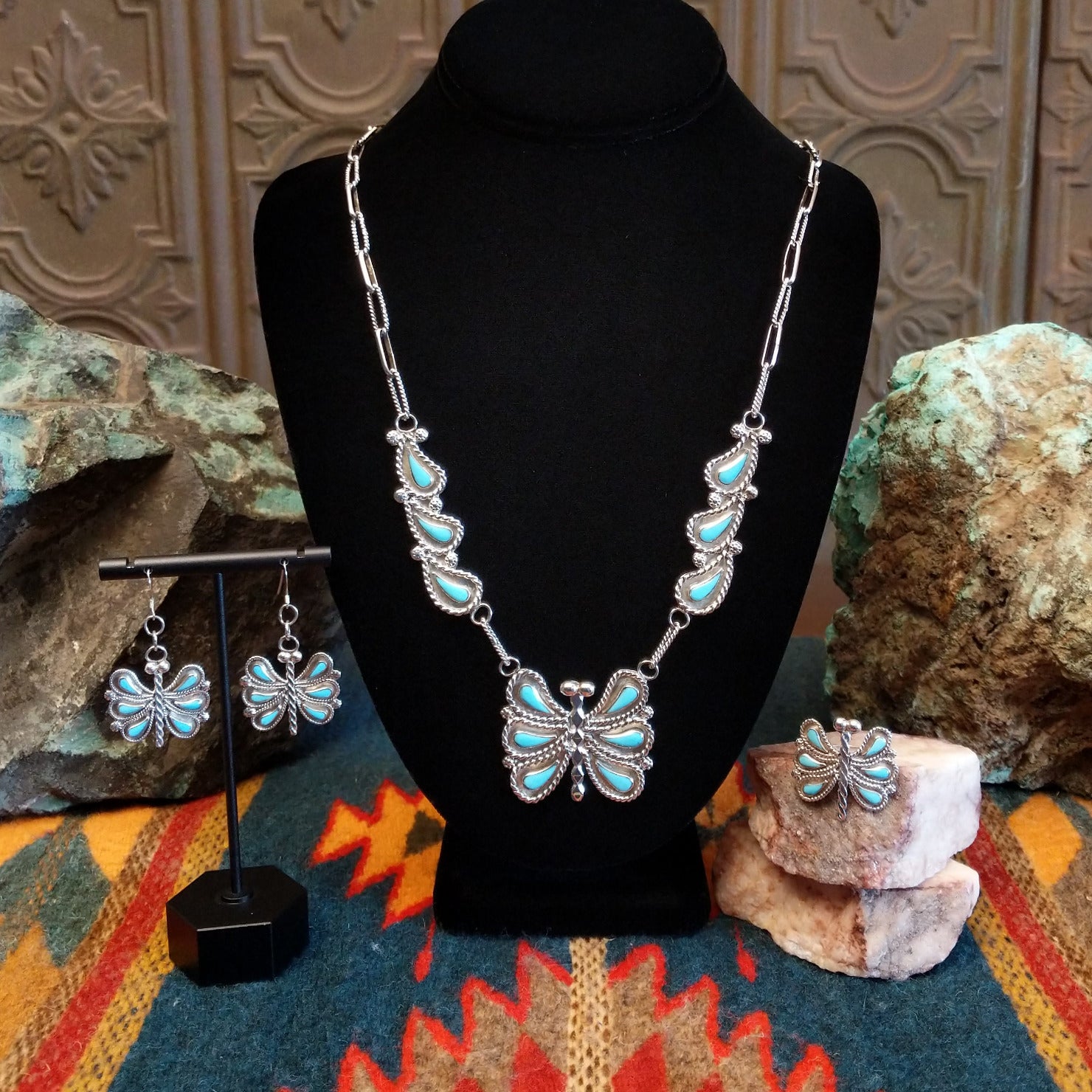 Butterfly-themed turquoise necklace and earrings, and ring on a black stand