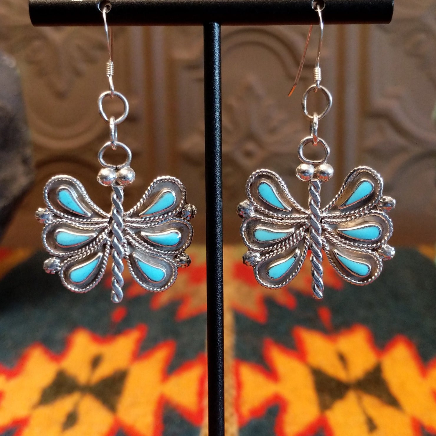 Butterfly-shaped earrings with turquoise on a stand.