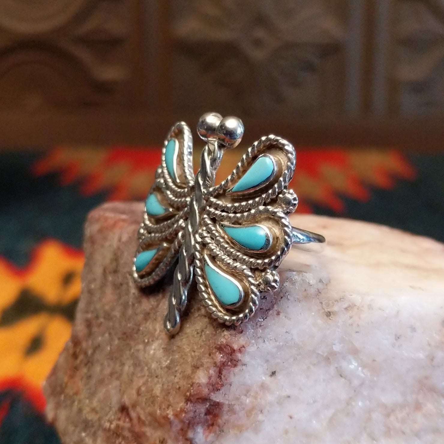 Butterfly-shaped silver and turquoise ring on a rock display, side view.