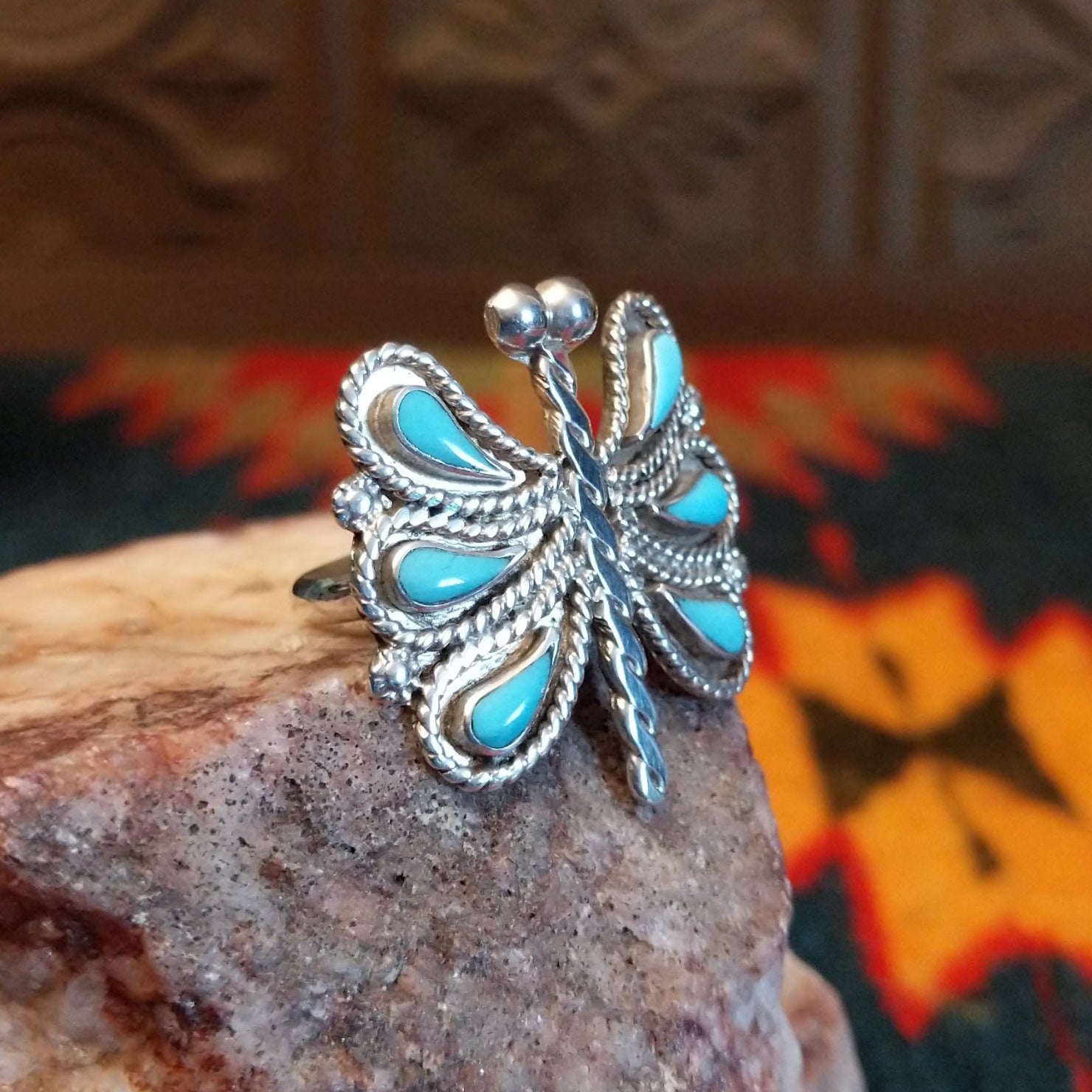 Butterfly-shaped silver and turquoise ring on a rock display, side view.