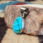Ovoid sterling silver pendant featuring a polished Sonoran Gold turquoise stone with blue-green color and golden matrix, handcrafted by Native American artist Fred Guerro Jr.  Side view.