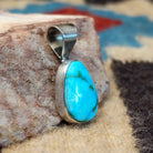Ovoid sterling silver pendant featuring a polished Sonoran Gold turquoise stone with blue-green color and golden matrix, handcrafted by Native American artist Fred Guerro Jr.  Side view.