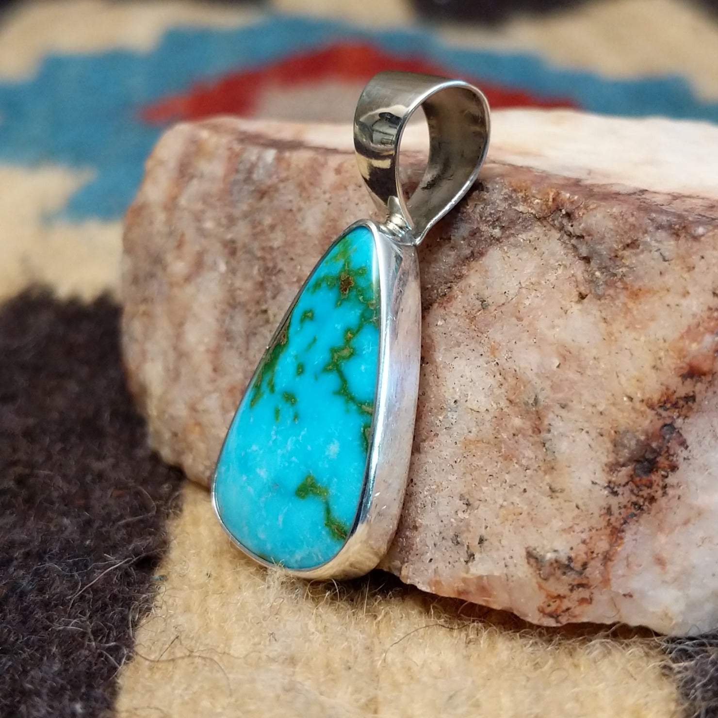 Teardrop sterling silver pendant featuring a polished Sonoran Gold turquoise stone with vivid blue-green color and natural golden matrix, handcrafted by Bernyse Chavez.  Side view.