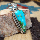 Deltoid-shaped sterling silver pendant featuring Sonoran Gold turquoise with vivid blue-green tones and natural golden matrix, handcrafted by Navajo artist Artie Yellowhorse.  Side view.