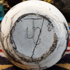 Small chiminea-style white horsehair pottery vase by local artisan Jim Calhoun with smoky natural patterns, polished finish, and handcrafted Southwestern design.  Underside view of artisan initials.