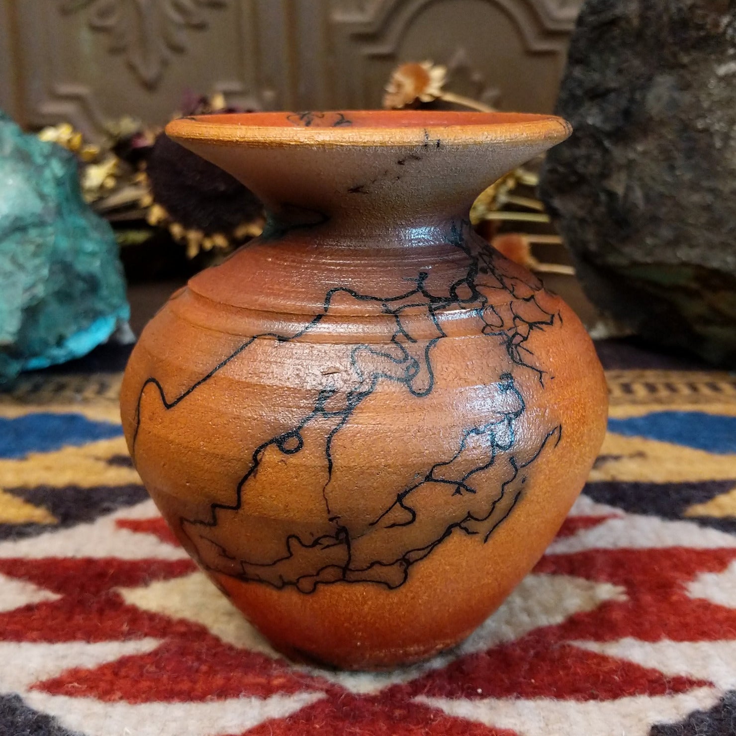 Small handcrafted terracotta horsehair vase with a rounded body and flared rim, decorated with black abstract horsehair firing patterns by artisan Jim Calhoun.