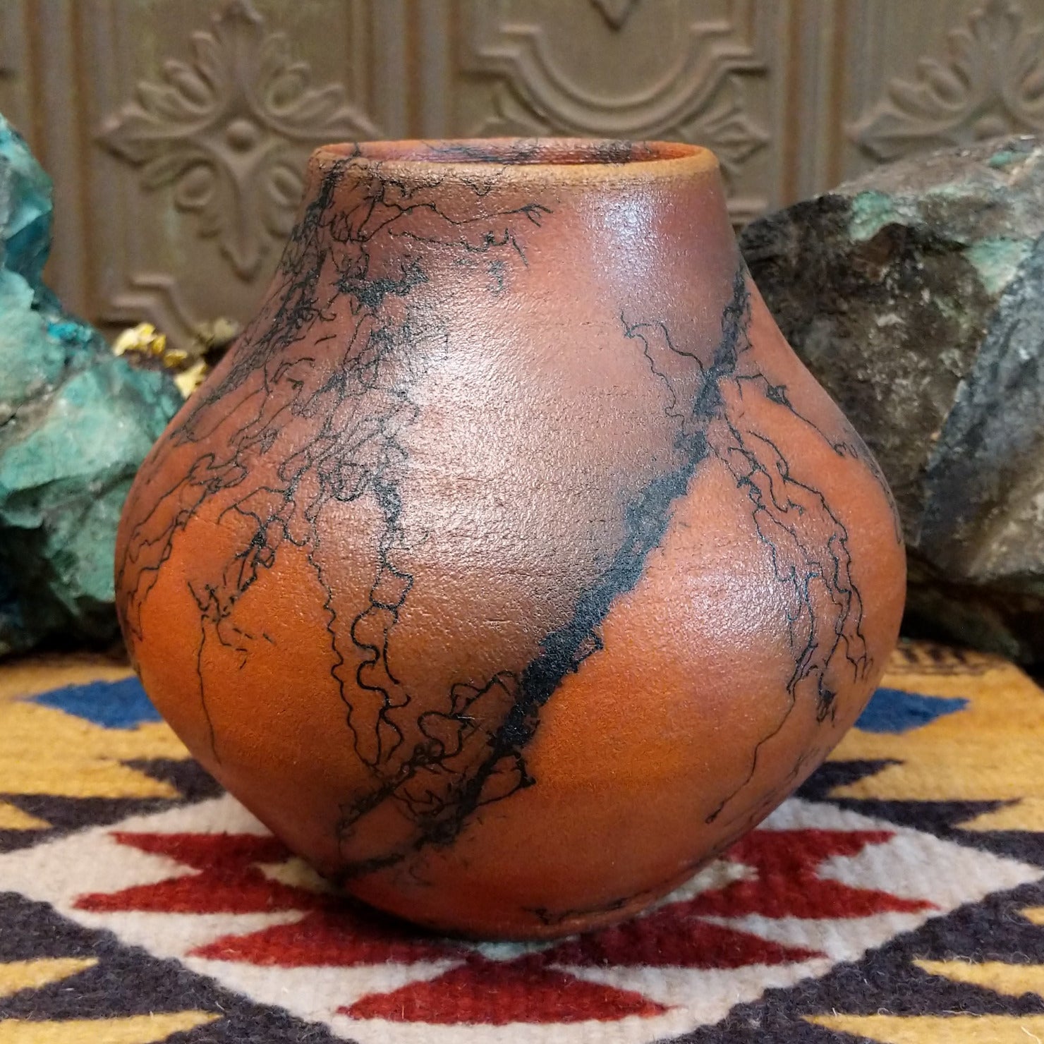 Medium-sized handcrafted terracotta horsehair pot with a rounded shape and flared opening, featuring black organic horsehair firing patterns on a warm terracotta finish by artisan Jim Calhoun.