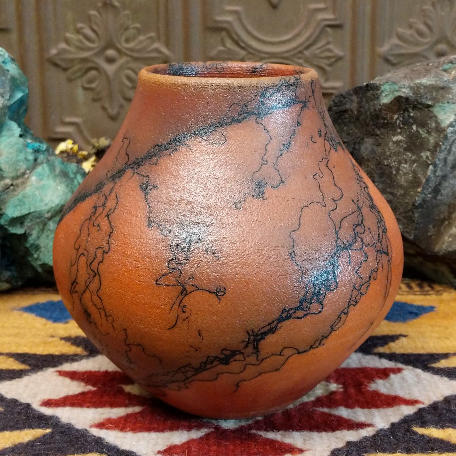 Medium-sized handcrafted terracotta horsehair pot with a rounded shape and flared opening, featuring black organic horsehair firing patterns on a warm terracotta finish by artisan Jim Calhoun.