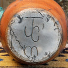 Flared terracotta horsehair vase handcrafted by local artisan Jim Calhoun, featuring a wide flared rim, earthy clay tones, and organic black horsehair fire patterns on the surface.  Underside view with artisan initials.