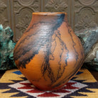 Large terracotta horsehair pottery vase by local artisan Jim Calhoun with rounded shape, warm clay tones, and distinctive black horsehair fire patterns across the surface.
