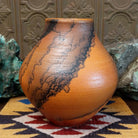 Large terracotta horsehair pottery vase by local artisan Jim Calhoun with rounded shape, warm clay tones, and distinctive black horsehair fire patterns across the surface.