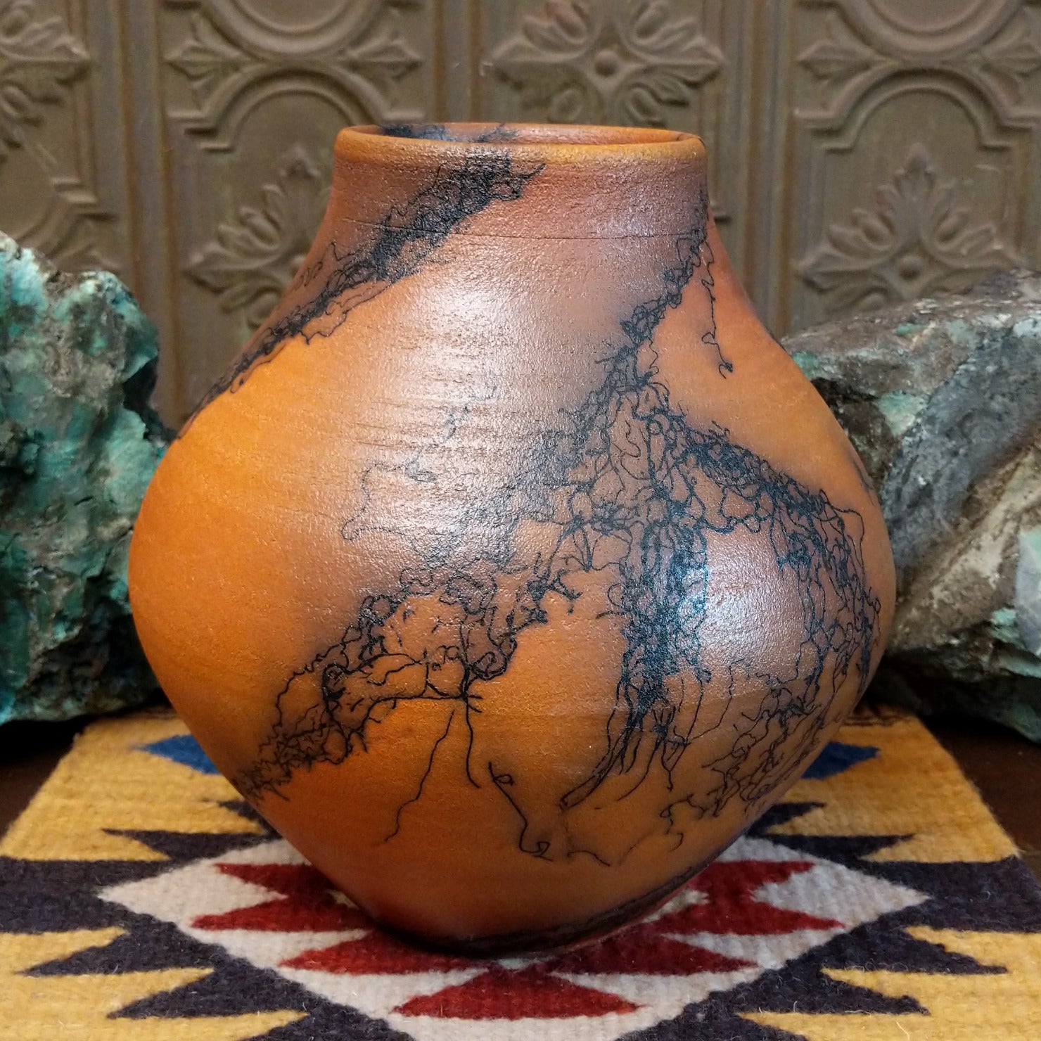 Large terracotta horsehair pottery vase by local artisan Jim Calhoun with rounded shape, warm clay tones, and distinctive black horsehair fire patterns across the surface.