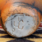 Small oval terracotta horsehair vase handcrafted by local artisan Jim Calhoun, featuring warm earthy clay tones and delicate black horsehair fire patterns on a smooth rounded surface.  Underside view with artisan initials.