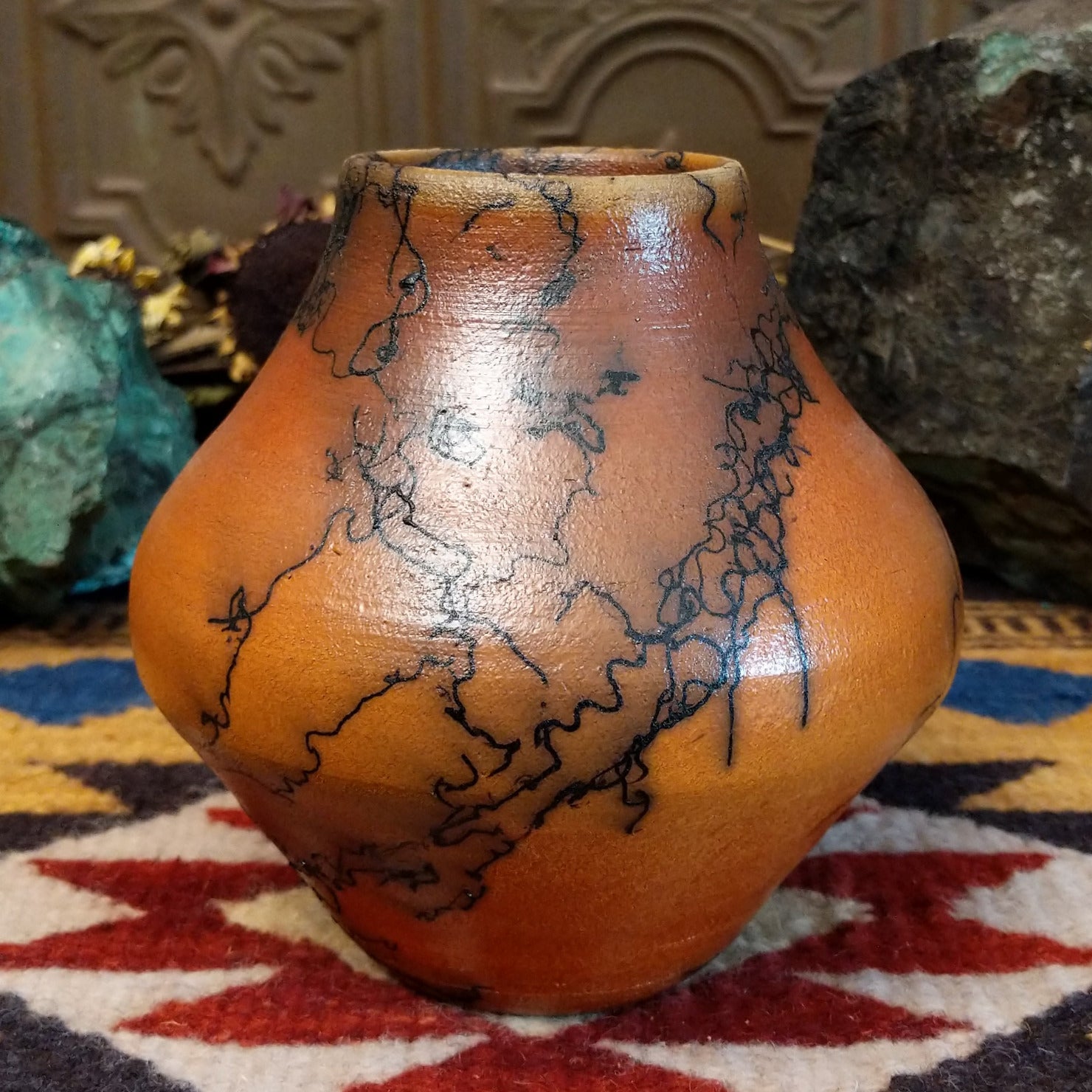 Small terracotta horsehair pot handcrafted by local artisan Jim Calhoun, featuring earthy clay tones and unique black horsehair fire patterns on a rounded pottery form.