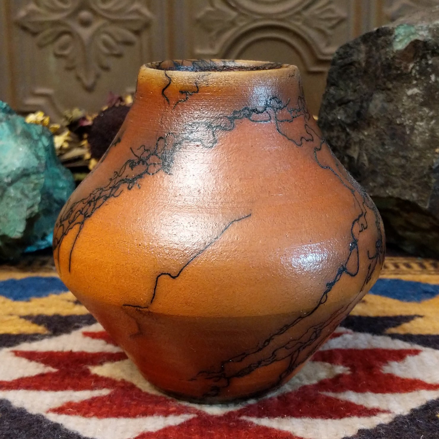 Small terracotta horsehair pot handcrafted by local artisan Jim Calhoun, featuring earthy clay tones and unique black horsehair fire patterns on a rounded pottery form.