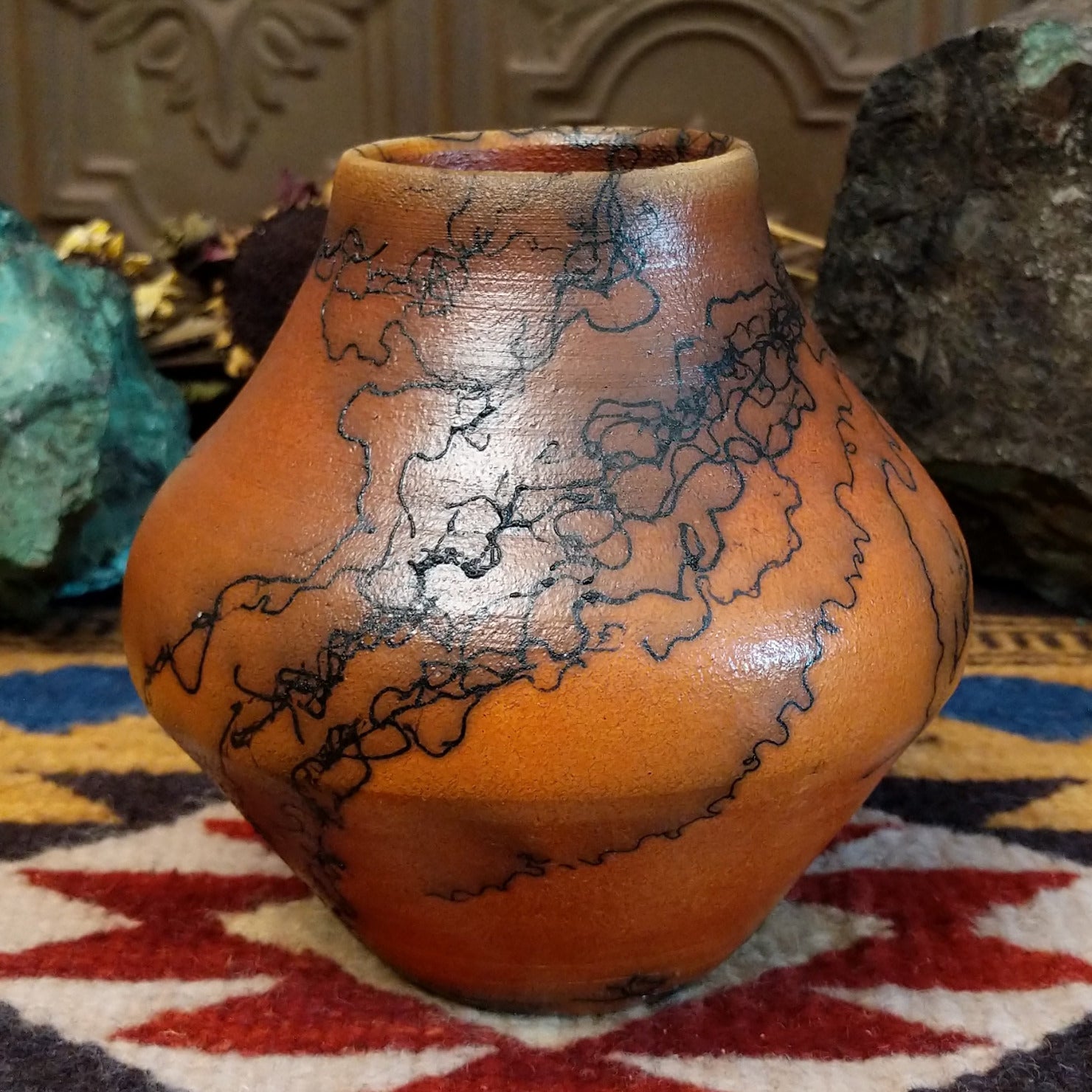 Small terracotta horsehair pot handcrafted by local artisan Jim Calhoun, featuring earthy clay tones and unique black horsehair fire patterns on a rounded pottery form.
