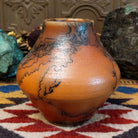 Small terracotta horsehair pot handcrafted by local artisan Jim Calhoun, featuring earthy clay tones and unique black horsehair fire patterns on a rounded pottery form.