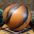 Large round terracotta horsehair pottery vessel handcrafted by local artisan Jim Calhoun, featuring warm clay tones and distinctive black horsehair fire patterns on a rounded surface.