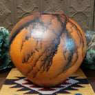Large round terracotta horsehair pottery vessel handcrafted by local artisan Jim Calhoun, featuring warm clay tones and distinctive black horsehair fire patterns on a rounded surface.