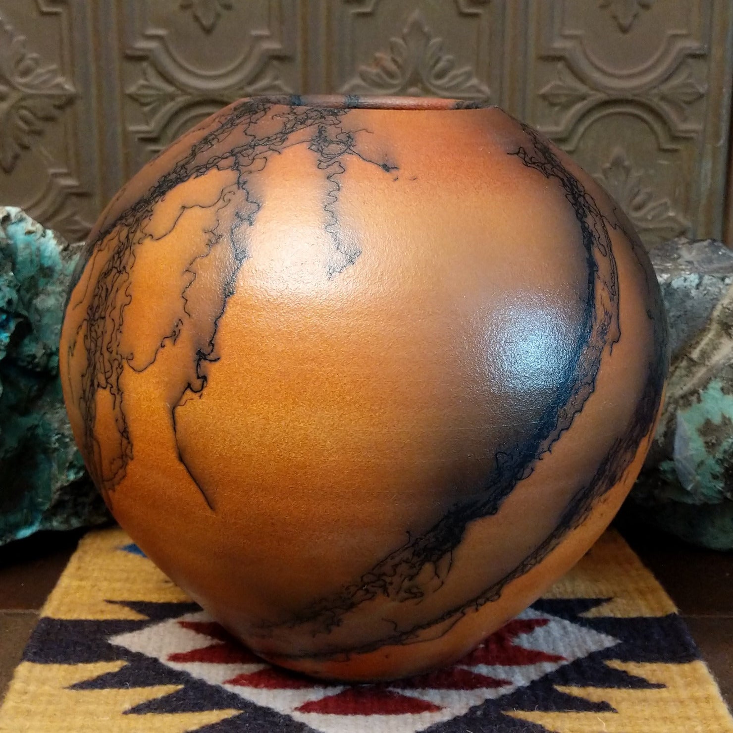 Large round terracotta horsehair pottery vessel handcrafted by local artisan Jim Calhoun, featuring warm clay tones and distinctive black horsehair fire patterns on a rounded surface.