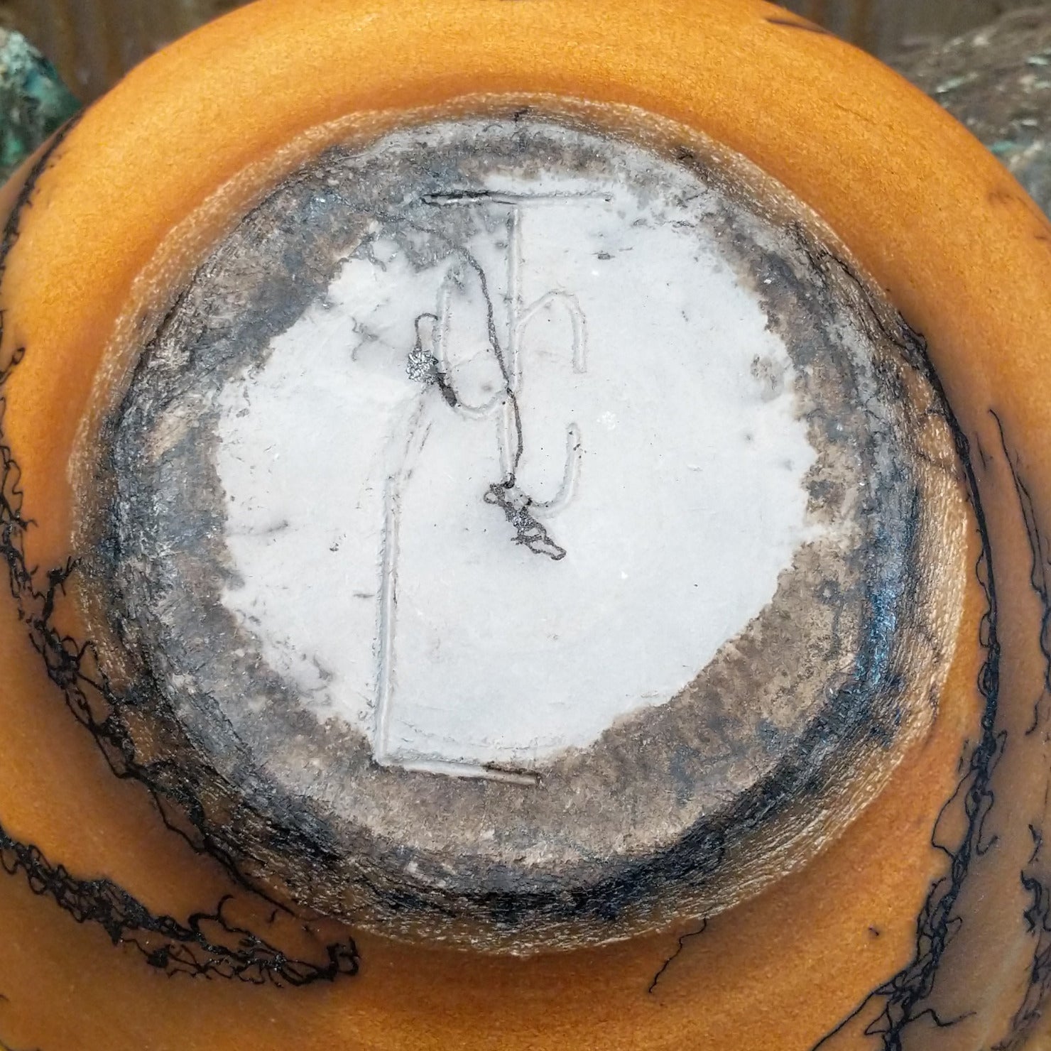 Large round terracotta horsehair pottery vessel handcrafted by local artisan Jim Calhoun, featuring warm clay tones and distinctive black horsehair fire patterns on a rounded surface.  Underside view with artisan initials.